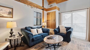 Un salon avec un canapé bleu, une table basse et une lampe. Il y a un tableau au mur et une fenêtre avec des rideaux.