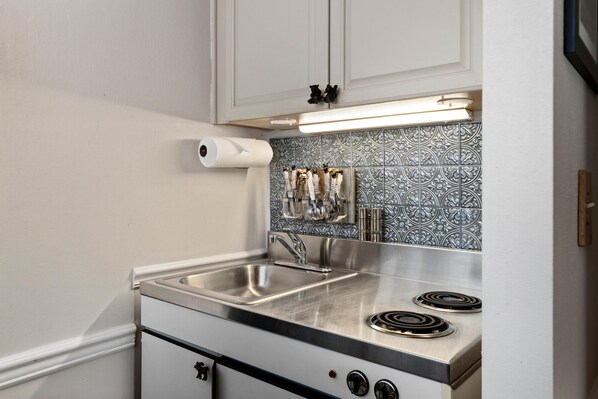 A compact kitchen with a stainless steel sink, a stove with a single burner, and a patterned backsplash.