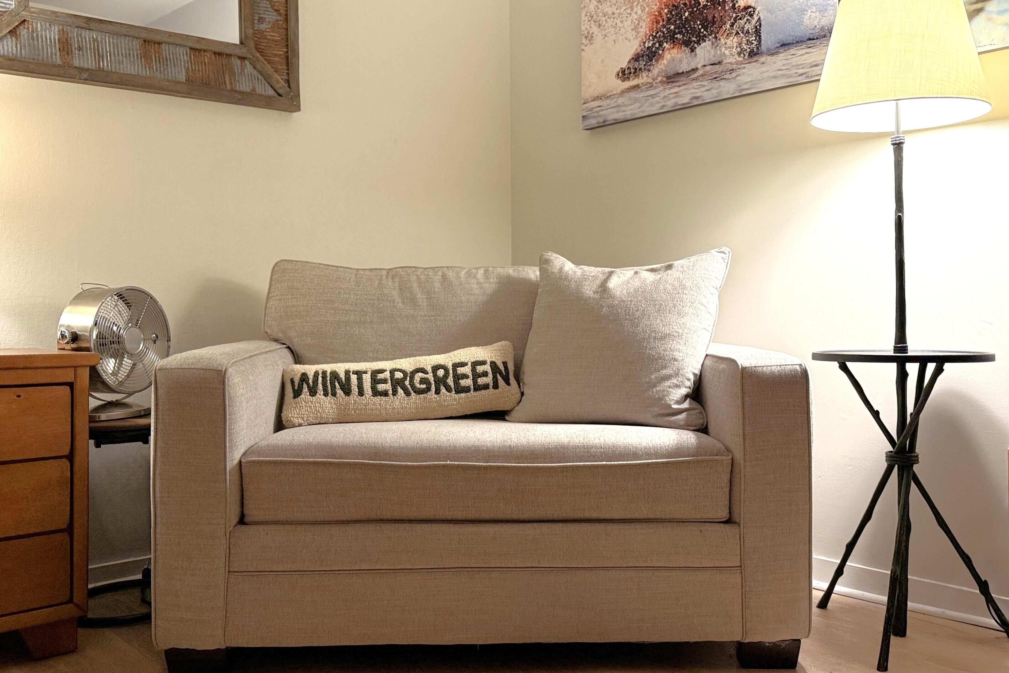 A beige sofa with a pillow labeled "WINTERGREEN" and a standing floor lamp.