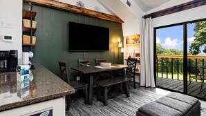 Una cocina moderna con televisor integrado, un comedor con mesa y bancos de madera, y un balcón con vistas al exterior.