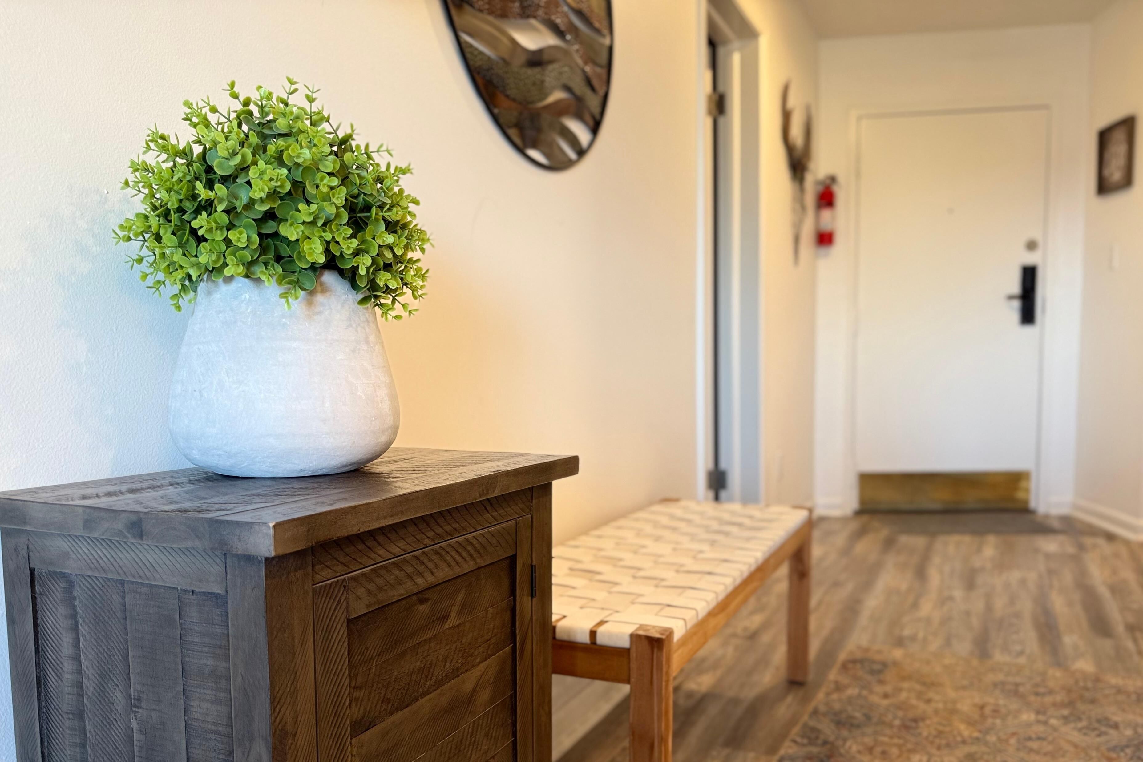 A hallway with a wooden bench, a potted plant, and a door at the end.