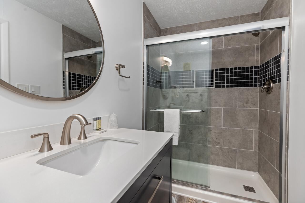 Un baño moderno con un lavamanos grande, dos grifos, un espejo y cabina de ducha con mampara de vidrio.