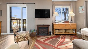 A living room with a flat-screen TV, a wooden cabinet, a patterned armchair, and a large window with curtains. - Timbers Lodge 49 with Wintergreen Advantage (Wintergreen)