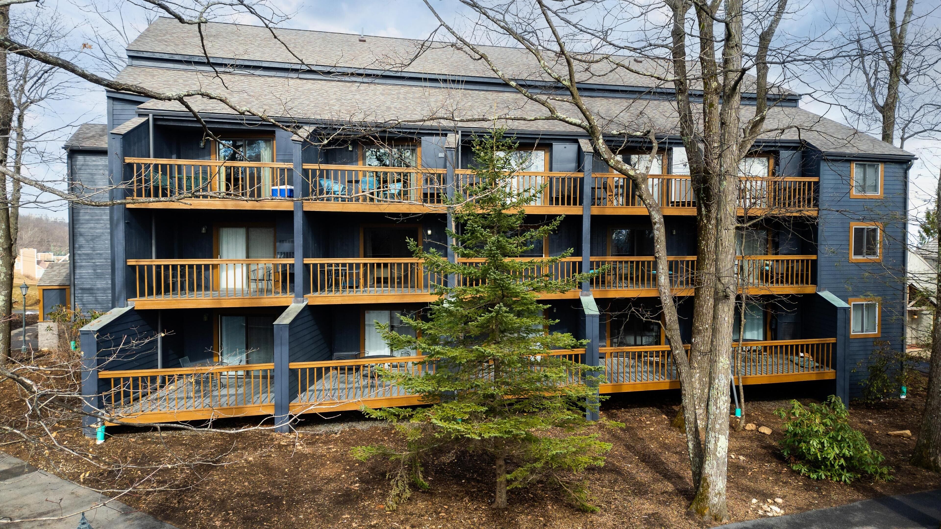 A multi-story building with balconies, a tree in front, and a clear sky.