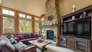 A cozy living room with a stone fireplace, a large TV, and a leather sofa. - Stunning Townhome with Great Views (Keystone)