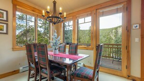 A dining area with a wooden table and plaid chairs, large windows with a view of trees, and a chandelier. - Stunning Townhome with Great Views (Keystone)