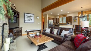 A spacious living area with a fireplace, a wooden coffee table, a leather sofa, and a kitchen in the background. - Stunning Townhome with Great Views (Keystone)