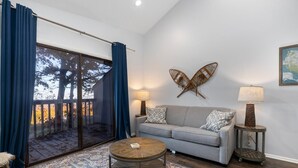 A living room with a grey sofa, a round coffee table, and a large window with blue curtains. - Timbers Lodge 57 with Wintergreen Advantage (Wintergreen)