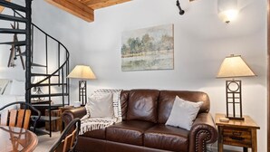 A living room with a brown leather sofa, wooden chairs, a spiral staircase, and two lamps on wooden side tables. - Mountain Inn Studio 53 with Wintergreen Advantage (Wintergreen)