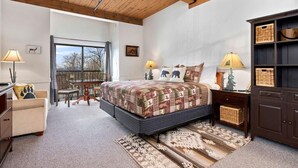 Ein Schlafzimmer mit einem großen Bett, Holzboden, einem Ausblick durch ein Fenster, einem kleinen Tisch und einem Bücherregal.