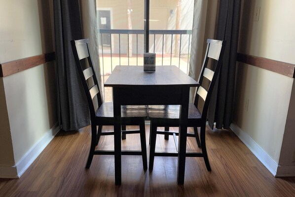 A dining area with a table and four chairs, a window with curtains, and a wooden floor.