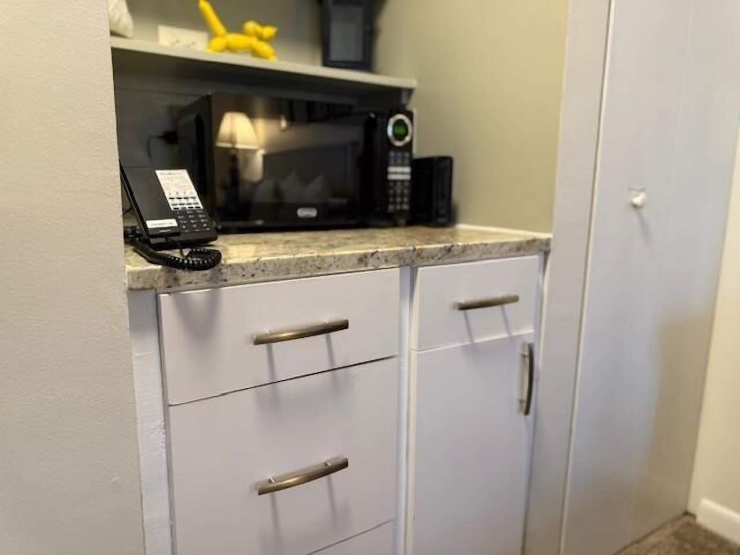 A kitchen with white cabinets, a microwave, a coffee maker, and a telephone on the countertop.