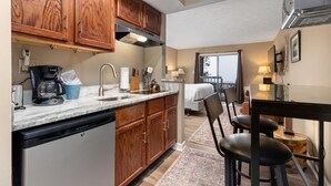 A compact kitchen with wooden cabinets, a dishwasher, and a coffee maker. There is a dining area with a table and chairs.