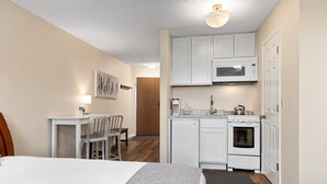 Une chambre d’hôtel compacte comprenant un lit, un bureau, une chaise et une kitchenette équipée d’un four à micro-ondes, d’une cuisinière et de placards.