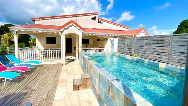 A poolside area with a covered patio, lounge chairs, and a swimming pool. - Villa Atoumo (Saint Anne)