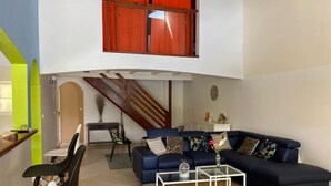 A living room with a blue sofa, a white coffee table, and a staircase with red railings. - Villa Atoumo (Saint Anne)