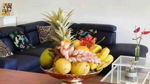 A fruit bowl on a wooden table in a living room with a blue sofa and patterned cushions. - Villa Atoumo (Saint Anne)