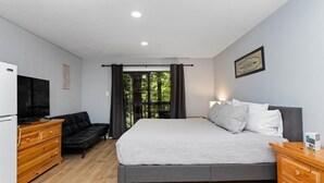 A bedroom with a bed, a TV, a dresser, a sofa, and a window with curtains. - Timbers Studio 18 with Wintergreen Advantage (Wintergreen)