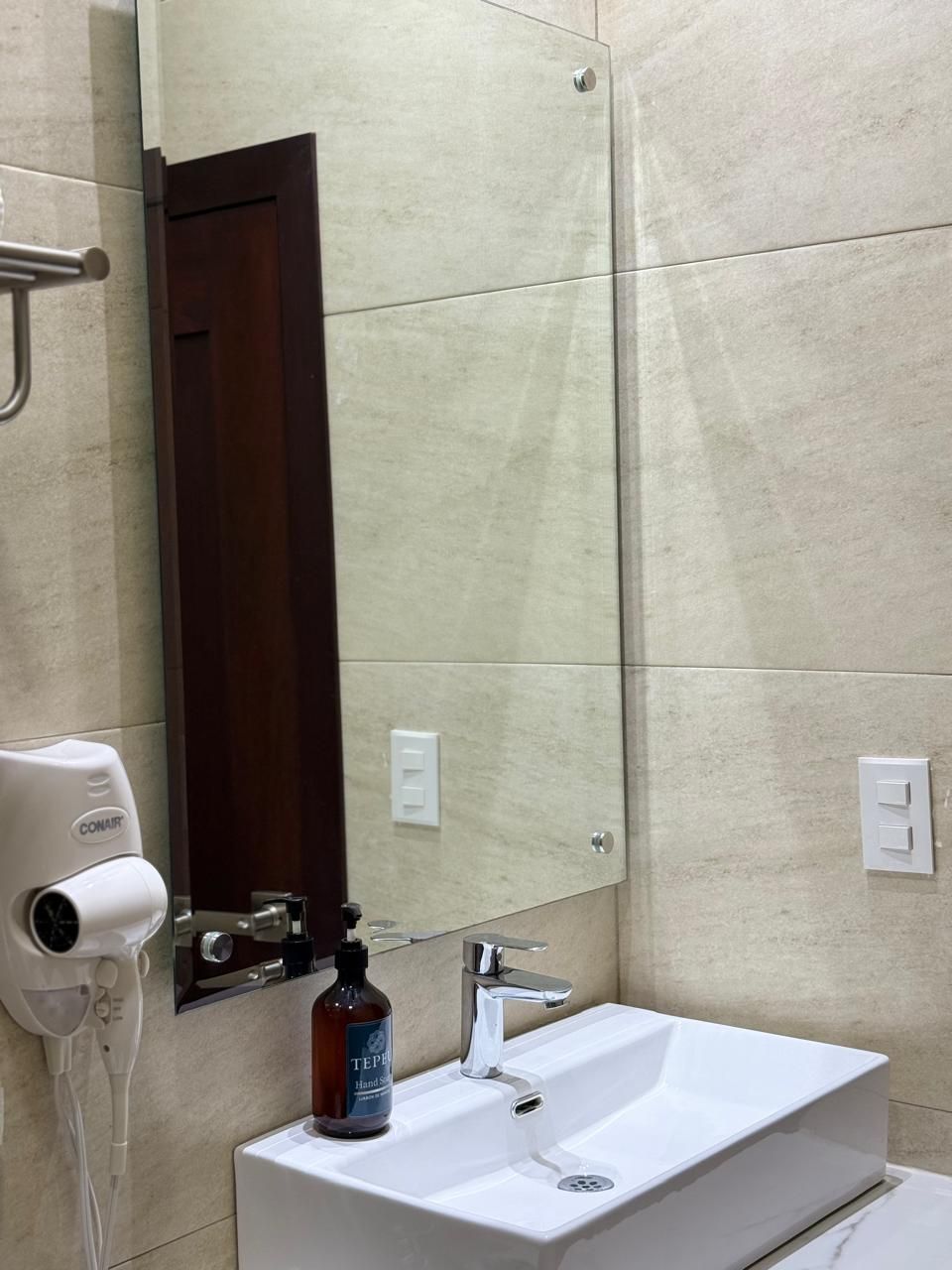 A bathroom with a white sink, a mirror, a hand dryer, and a bottle of hand soap.