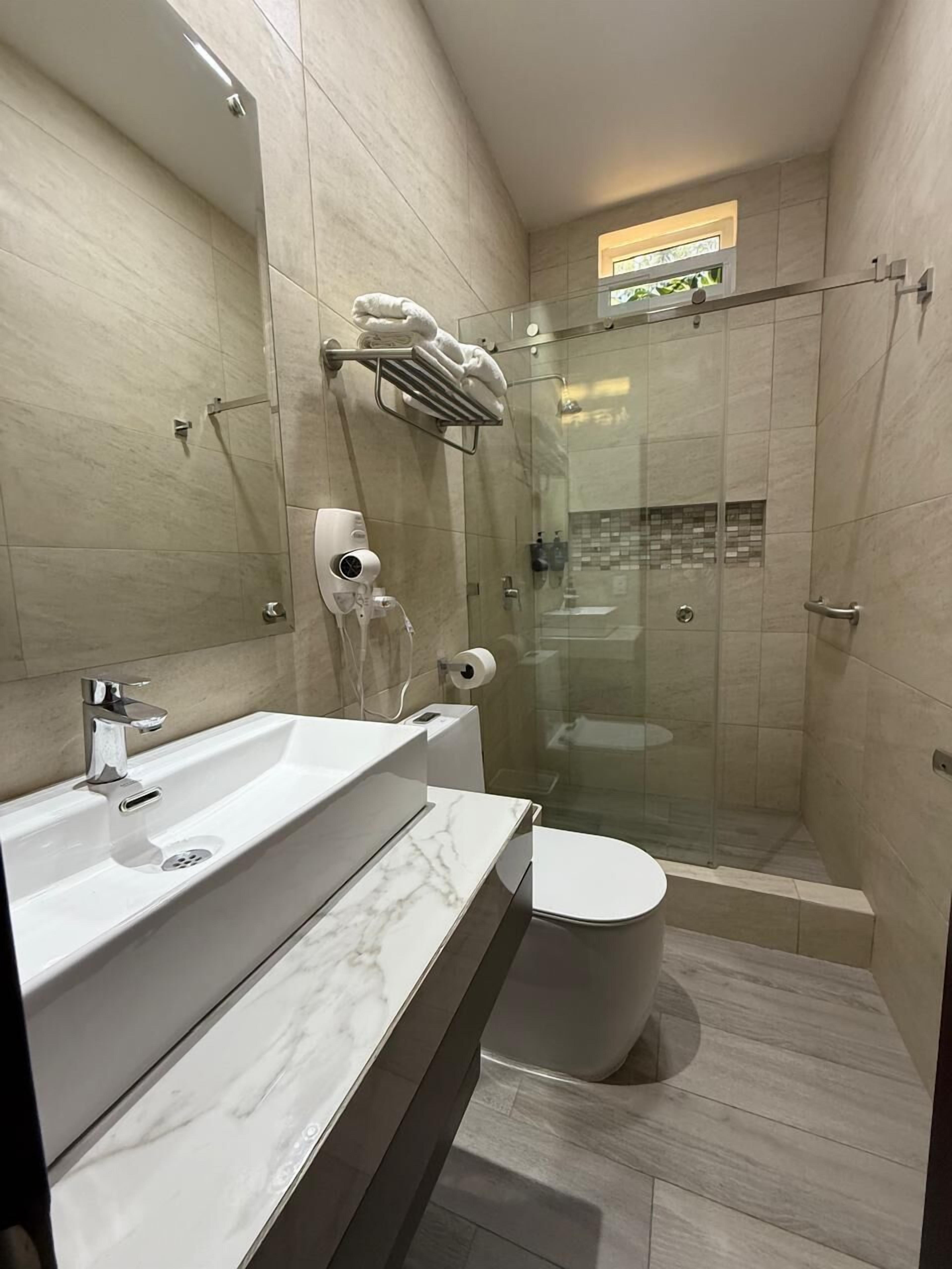 Un baño moderno con cabina de ducha de vidrio, lavamanos blanco y un inodoro.