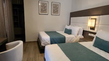 Quarto de hotel com duas camas, um ventilador de teto, uma escrivaninha e uma cadeira.