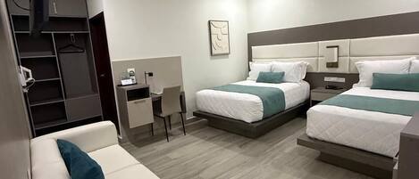 A modern hotel room with a sofa, two beds, a desk, and a ceiling fan.