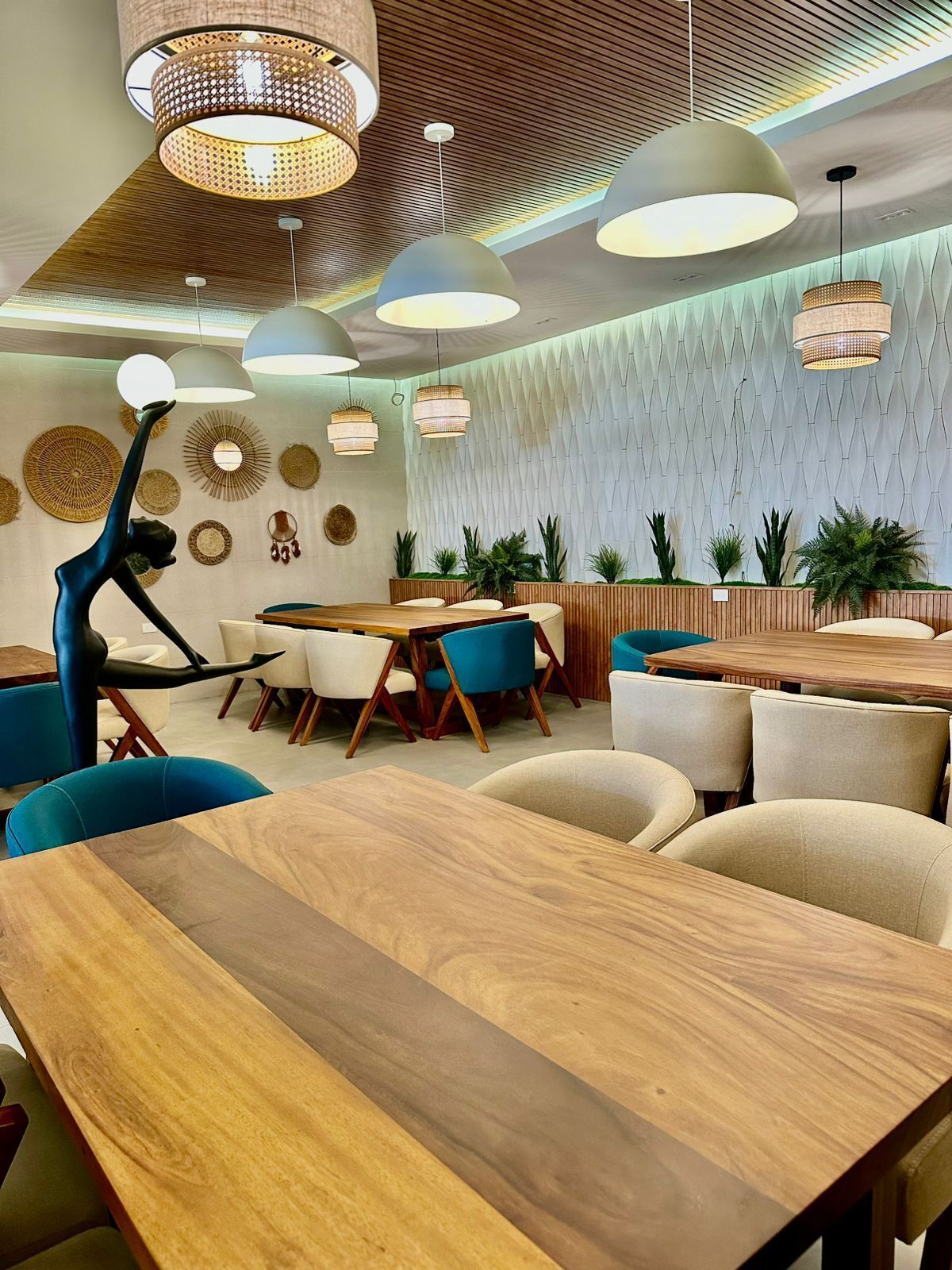 Interior moderno de restaurante con mesas y sillas de madera, lámparas colgantes y paneles decorativos en la pared.
