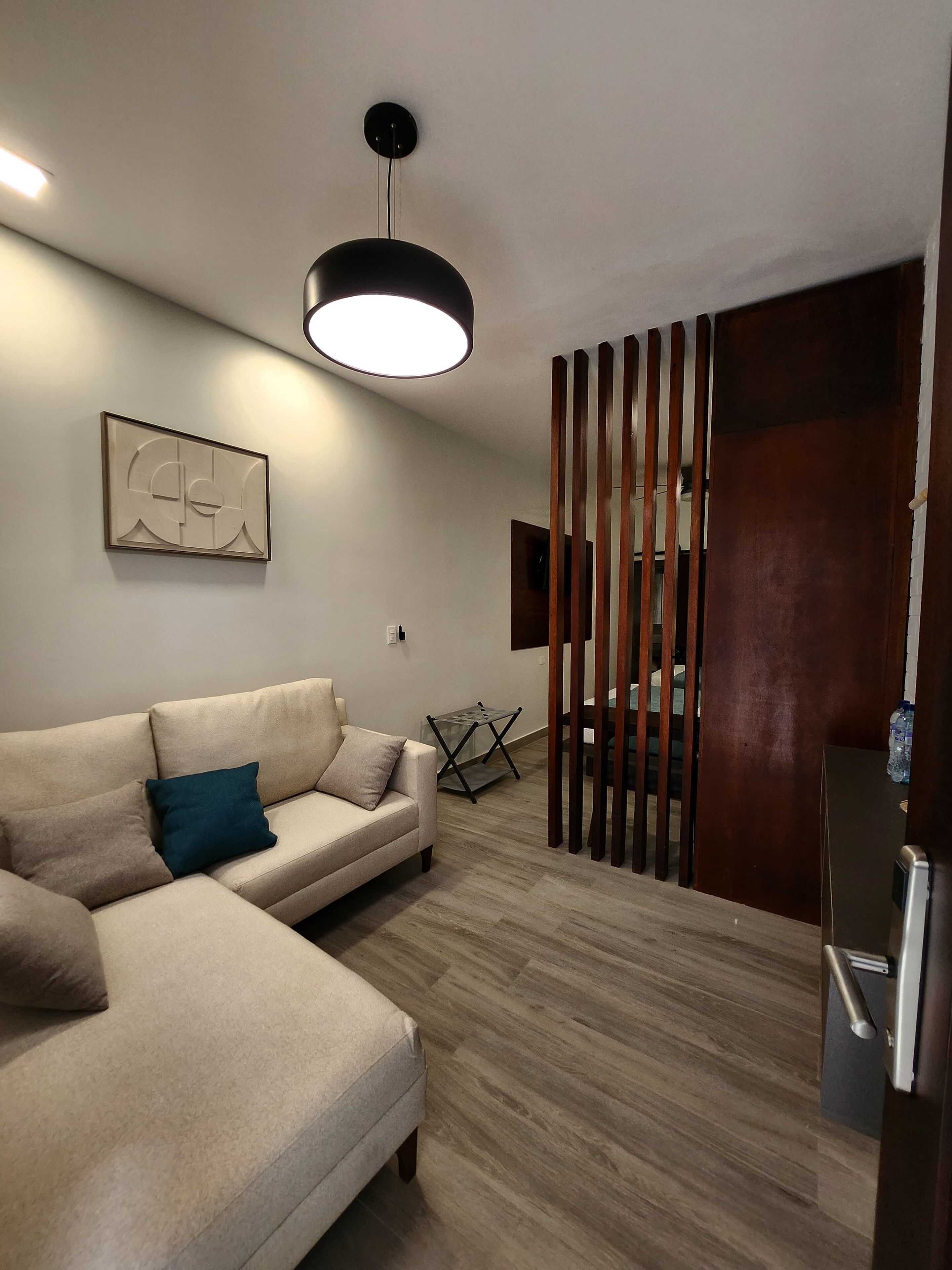 A modern living room with a beige sectional sofa, a black pendant light, a wooden partition, and a framed abstract artwork on the wall.