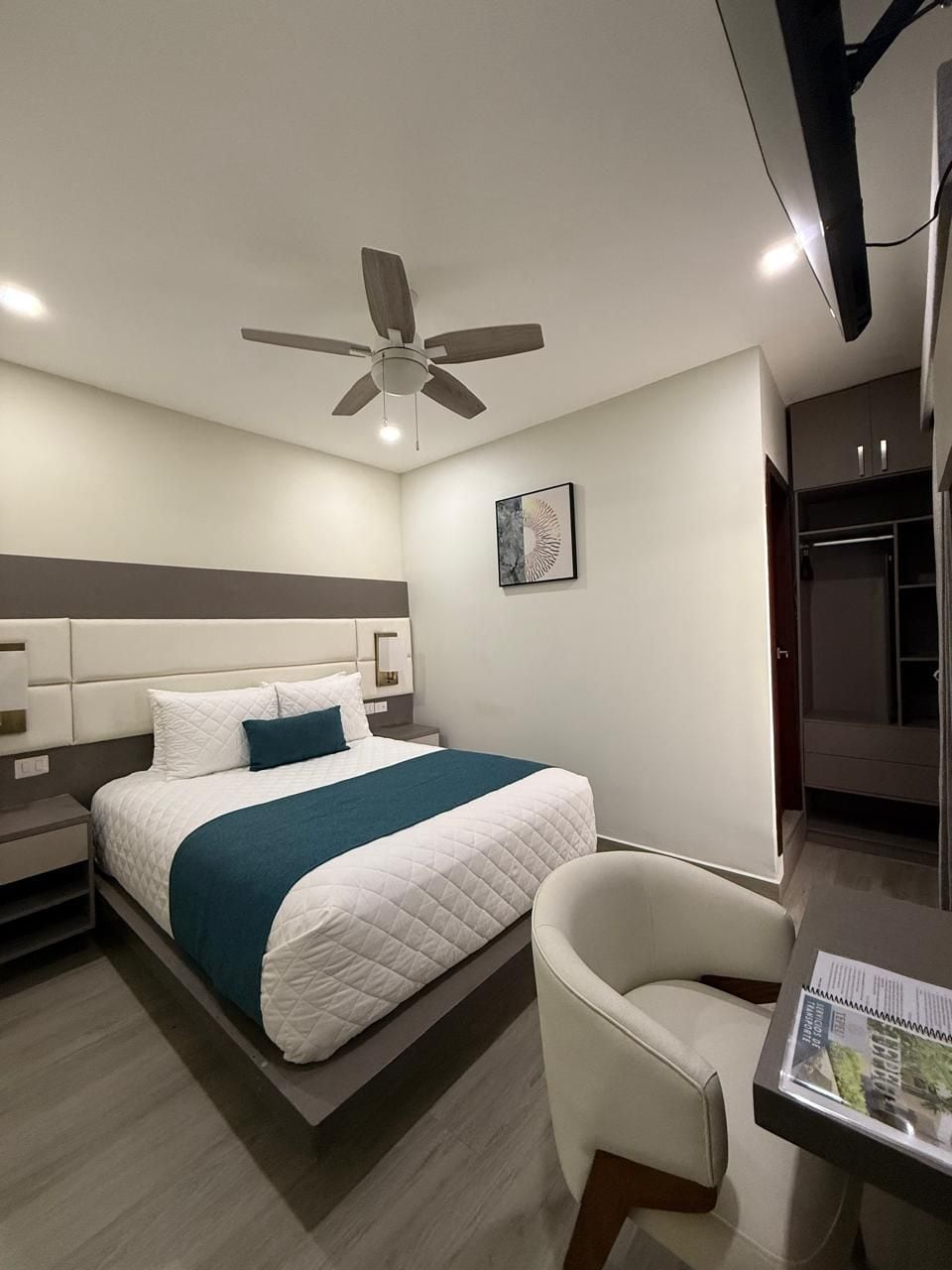 A modern bedroom with a bed, a chair, a desk, and a ceiling fan.