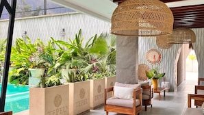 A modern lounge area with wooden furniture, a pool, and lush greenery. - Hotel Tepeu (Flores)