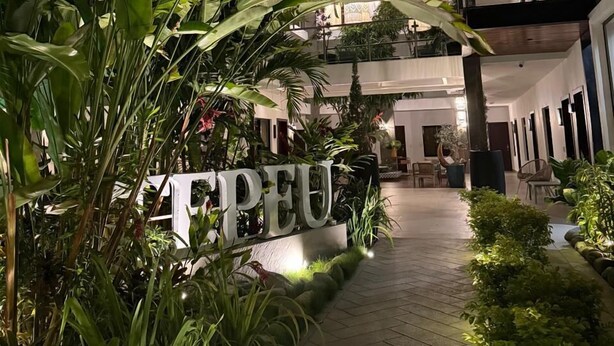 A modern hotel atrium with a central pathway, surrounded by lush greenery and a large sign reading "PEU". - Hotel Tepeu (Flores)