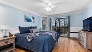 Ein Schlafzimmer mit Bett, Nachttisch, Kommode, Fernseher und Blick ins Freie durch eine Schiebetür.
