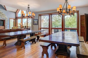Un'ampia sala da pranzo con tavoli e panche in legno, ampie finestre che si affacciano su alberi e un camino in pietra.