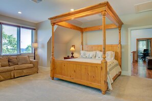 Un letto a baldacchino con struttura in legno, un divano color beige e una lampada su un comodino.