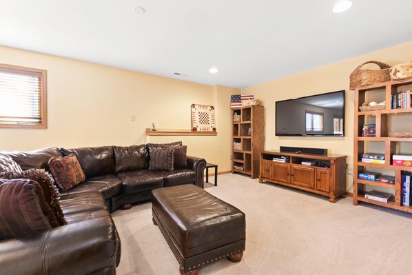 A living room with a leather sectional sofa, ottoman, wooden entertainment center, and a flat-screen TV.