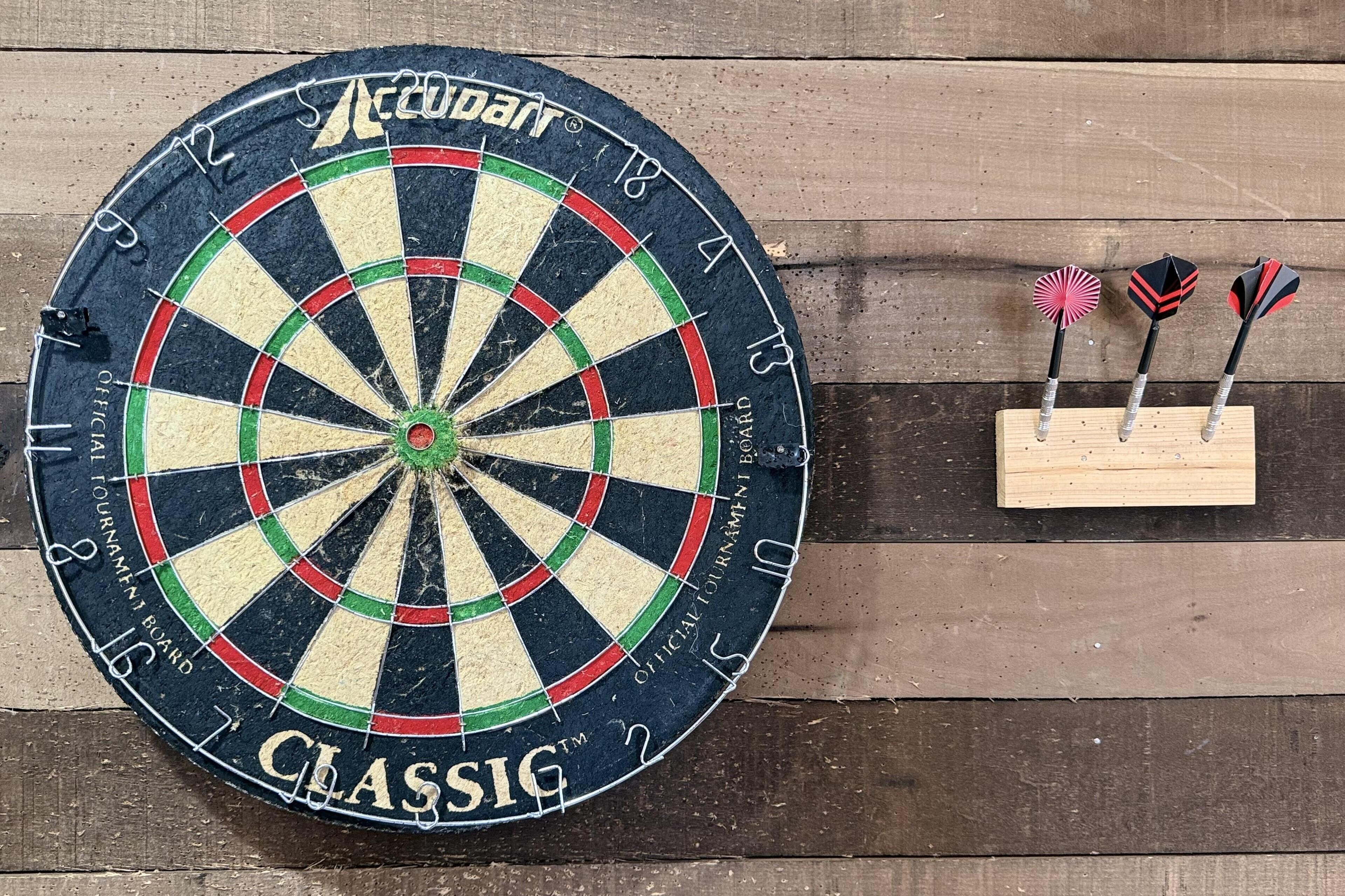 A dartboard with three darts stuck in it, mounted on a wooden wall.