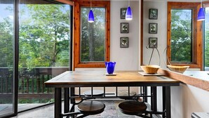 A modern kitchen with large windows, a wooden table, and hanging pendant lights.