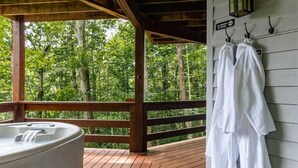 A wooden deck with a hot tub, a wooden railing, and a wall-mounted towel rack with towels.