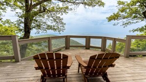 Deux fauteuils Adirondack sur une terrasse en bois, avec vue sur un paysage montagneux.