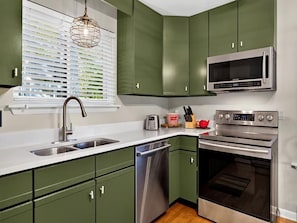 A kitchen with green cabinets, a stainless steel microwave, a toaster, and a dishwasher.