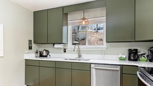 Une cuisine moderne avec des meubles de couleur verte, un évier en acier inoxydable et un lave-vaisselle.