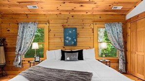 Une chambre dans une cabane en bois, avec un lit, deux tables de chevet, une horloge et des rideaux.