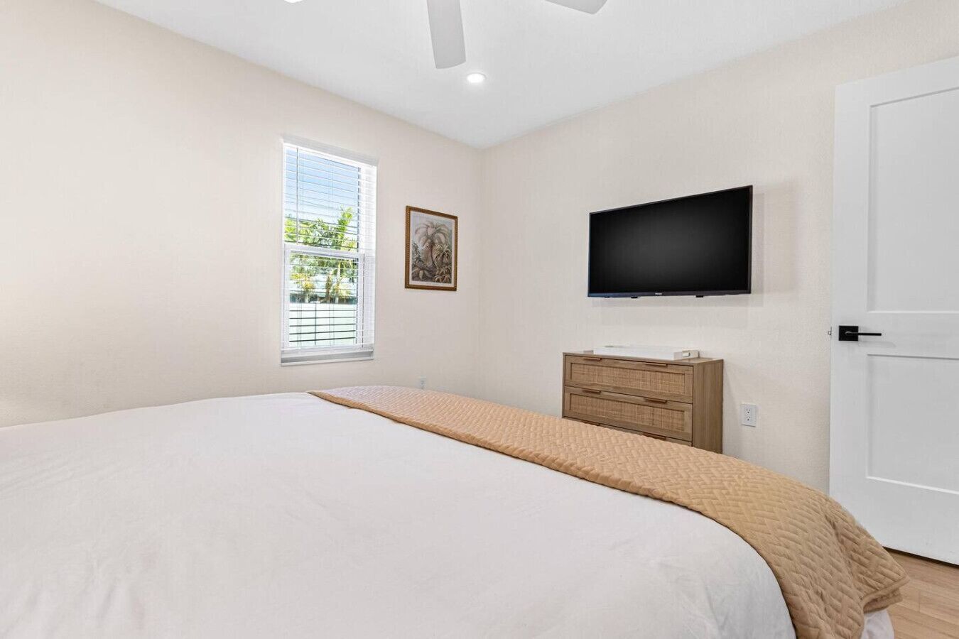 Un dormitorio con una cama grande, un televisor en la pared, una ventana con persianas y una puerta.