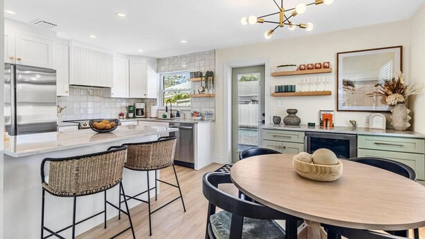 A modern kitchen with white cabinetry, a central island, and a dining area with a round table and chairs.
