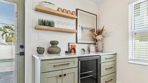 A kitchen with light green cabinets, a stainless steel oven, and a white countertop. There are shelves above the cabinets holding decorative items and glasses.