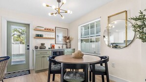 A modern kitchen with a round dining table, two chairs, a chandelier, and a large mirror.