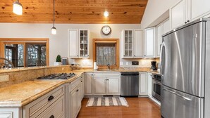 A modern kitchen with white cabinets, stainless steel appliances, a wooden ceiling, and a clock on the wall. - Chestnut Springs with Wintergreen Advantage (Wintergreen)