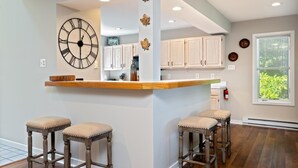 Una cocina con una isla central, taburetes de madera y un gran reloj de pared.