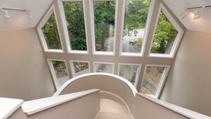 Una escalera moderna con diseño curvo que lleva a un balcón con amplios ventanales y vistas a una zona boscosa.