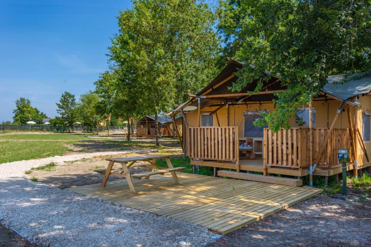 Une cabane en bois dotée d’une terrasse, entourée d’arbres et agrémentée d’une table de pique-nique.